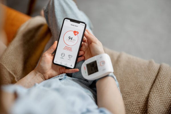 Woman measure heart rate and pressure with smart technology in phone while sitting on sofa at home. Health and wellness concept.